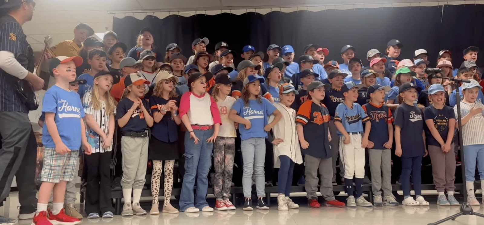 Students and staff on stage singing in baseball costumes
